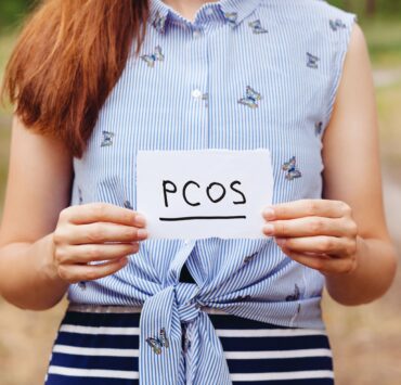 Zespół policystycznych jajników - kobieta trzymająca w rękach kartkę z napisem "PCOS"