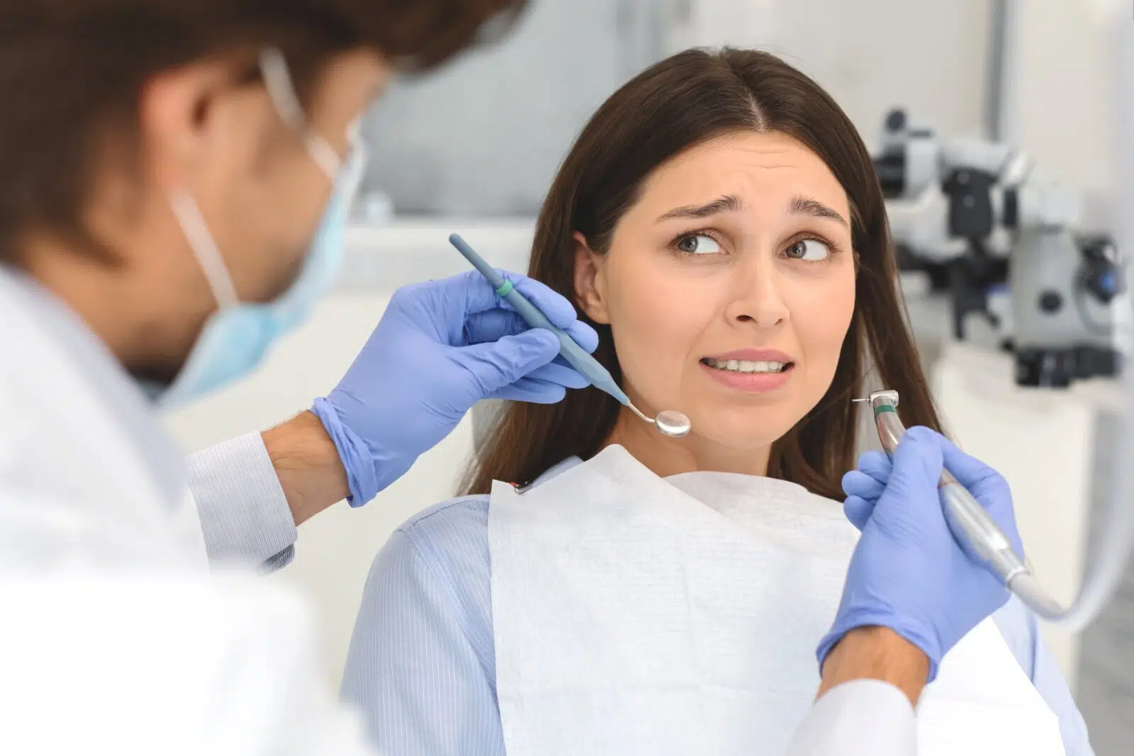 Strach przed dentystą - przestraszona kobieta na fotelu dentystycznym patrząca na stomatologa