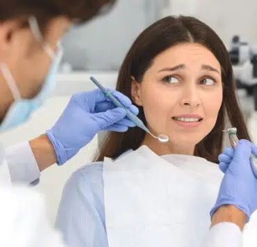 Strach przed dentystą - przestraszona kobieta na fotelu dentystycznym patrząca na stomatologa